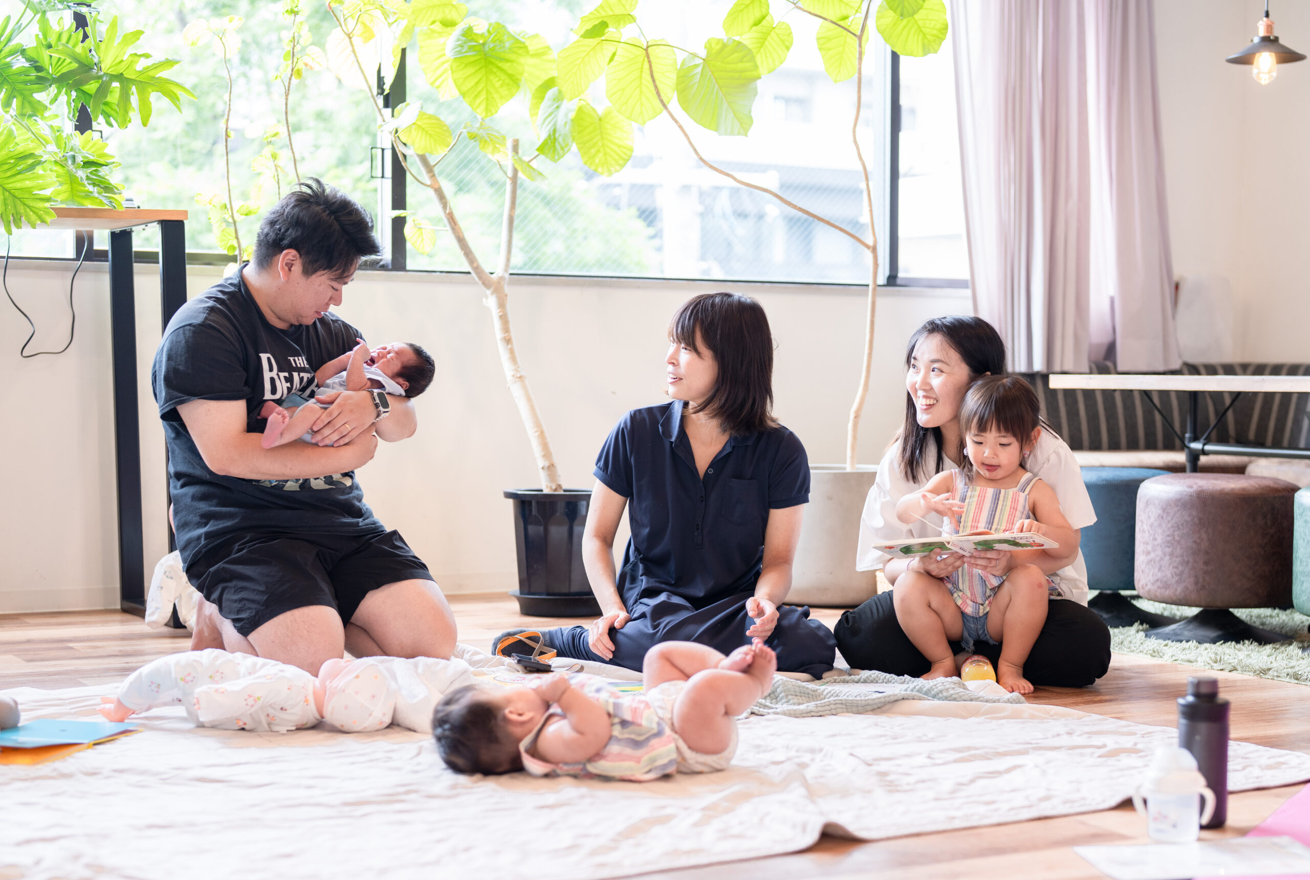 明るい室内に集まり、子どもたちと一緒に過ごす親子と支援者